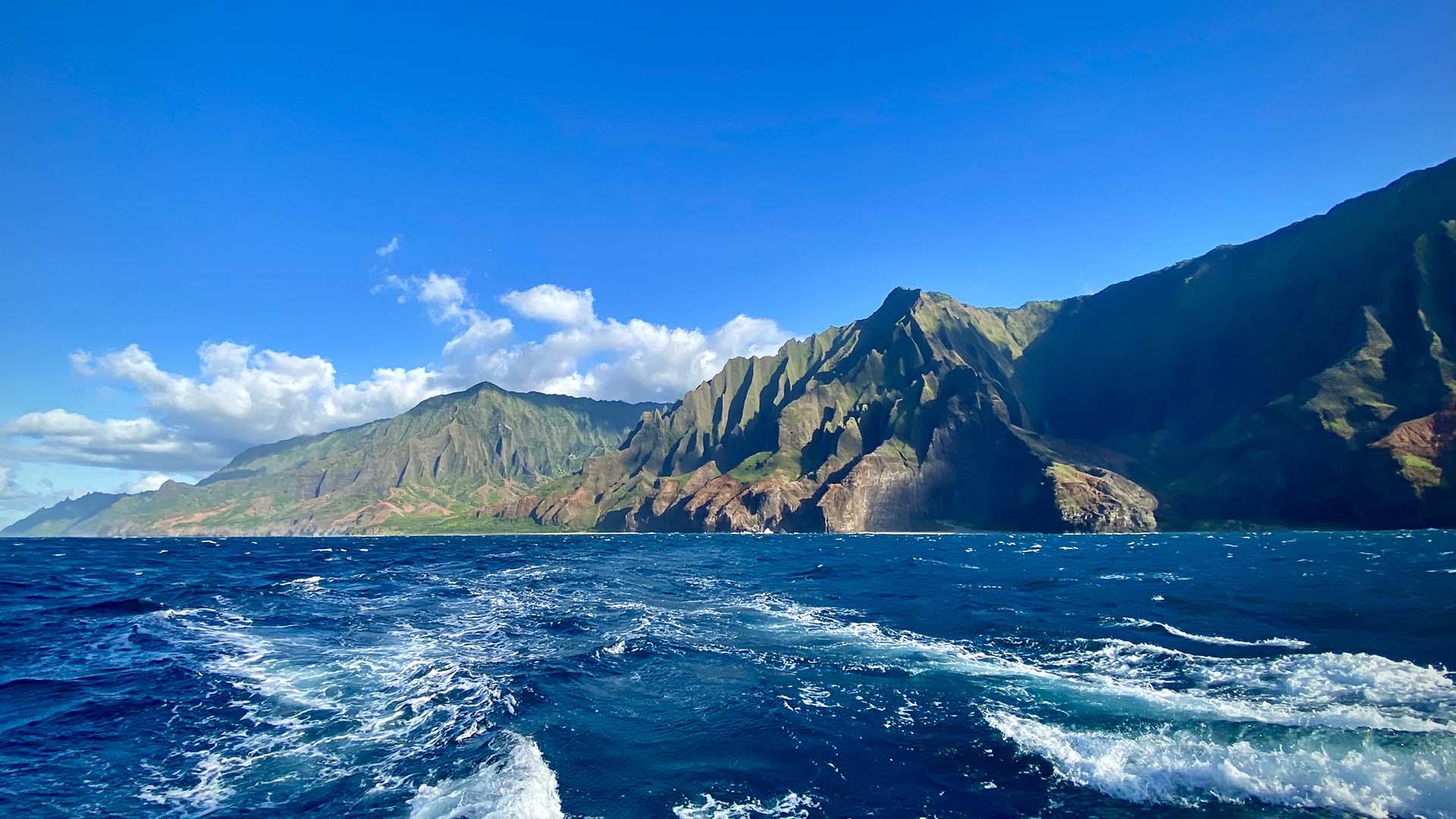 Ocean waves off a green coastal mountain range