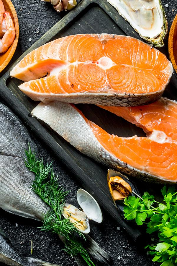 Salmon steaks, shellfish, and herbs arranged on a dark board