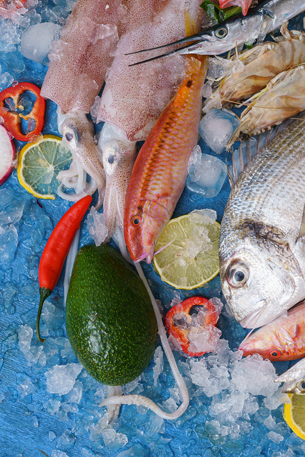 Assorted seafood including squid, fish, and shellfish displayed on ice with avocado, chili peppers, and lime slices