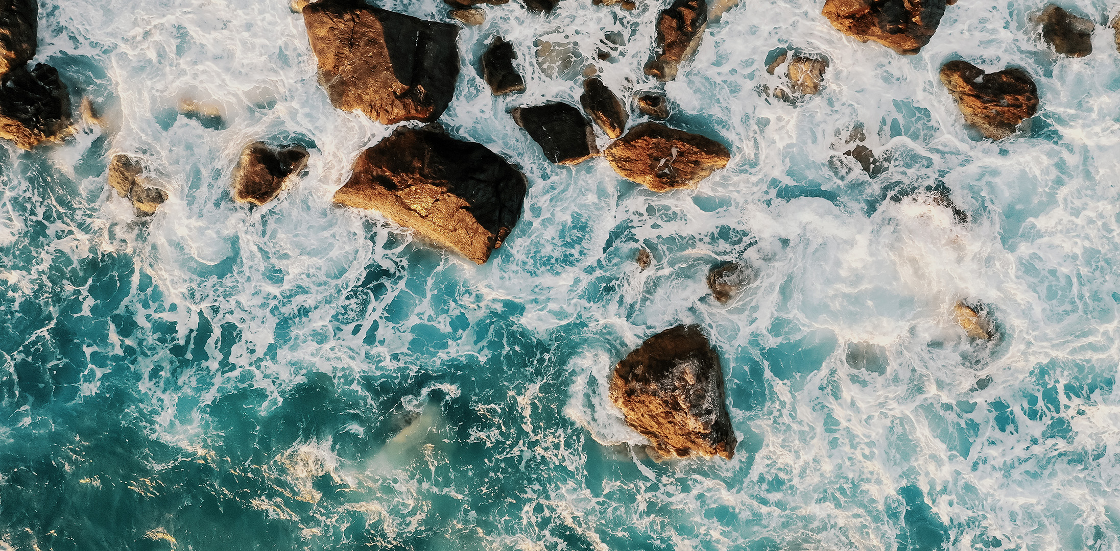 Aerial view of ocean waves crashing against large rocks along the coastline